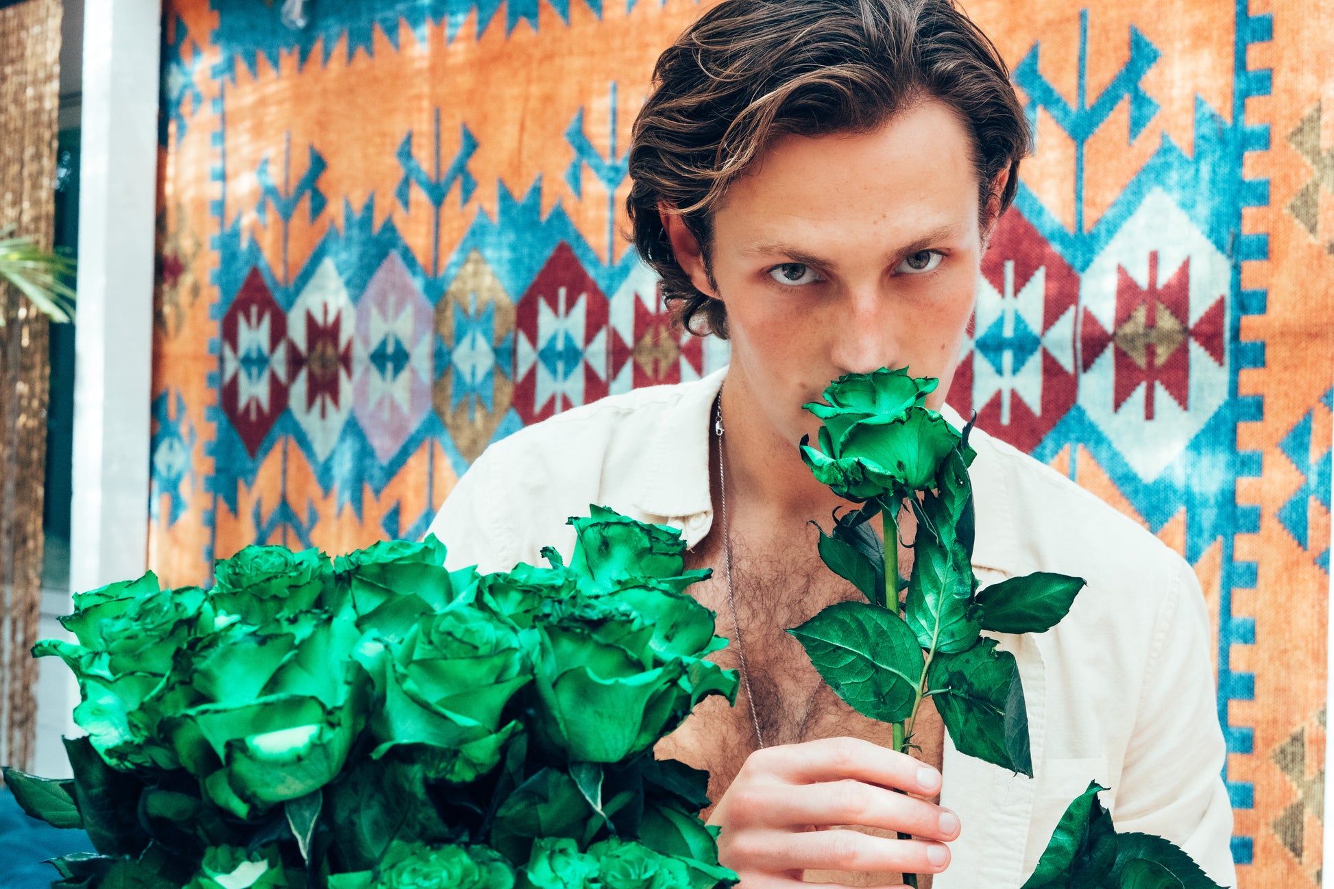 Man holding green roses in front of a colorful patterned background