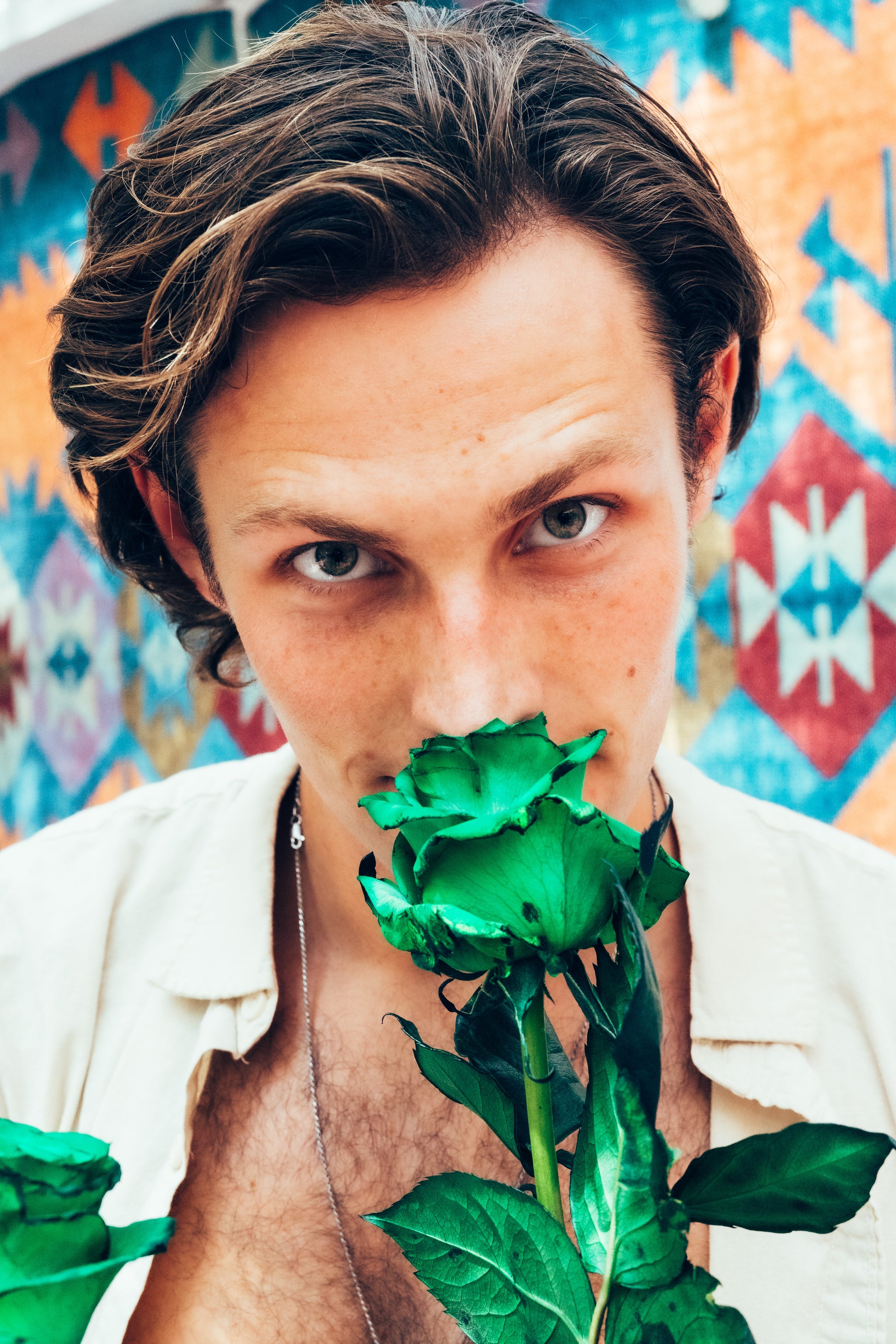 Person holding green roses in front of a colorful geometric background