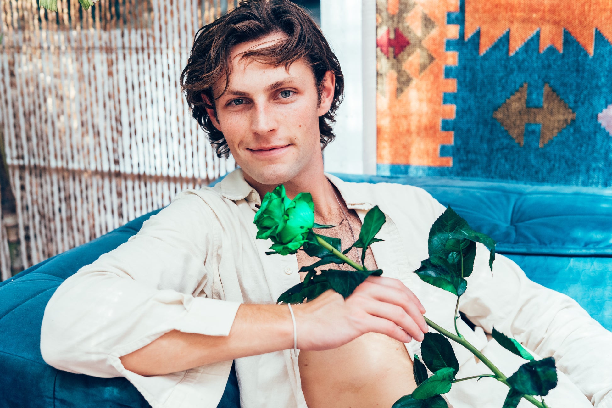 Man holding a green rose in an indoor setting with a colorful rug in the background