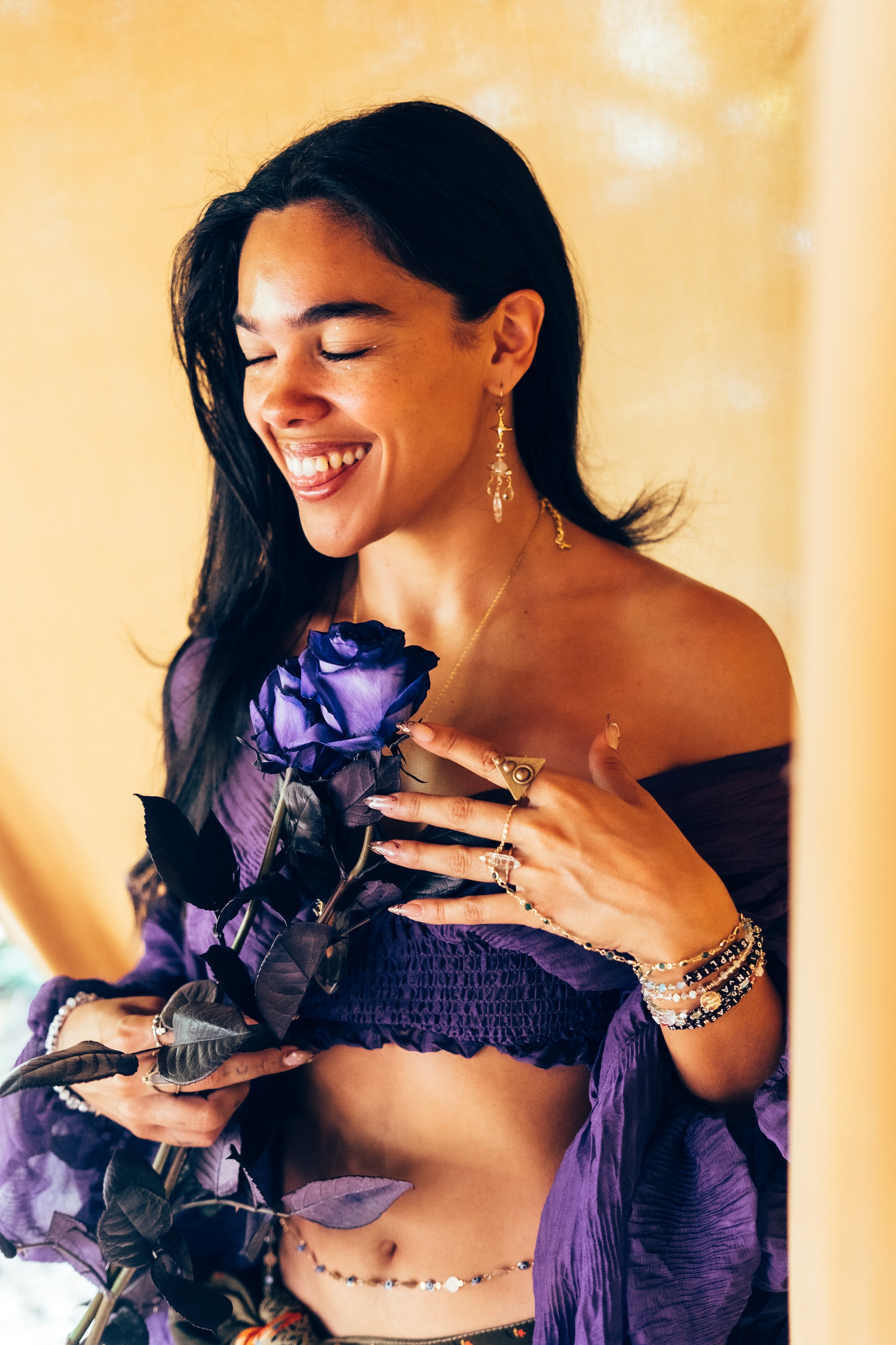 Woman in a purple outfit holding a purple flower against a yellow background