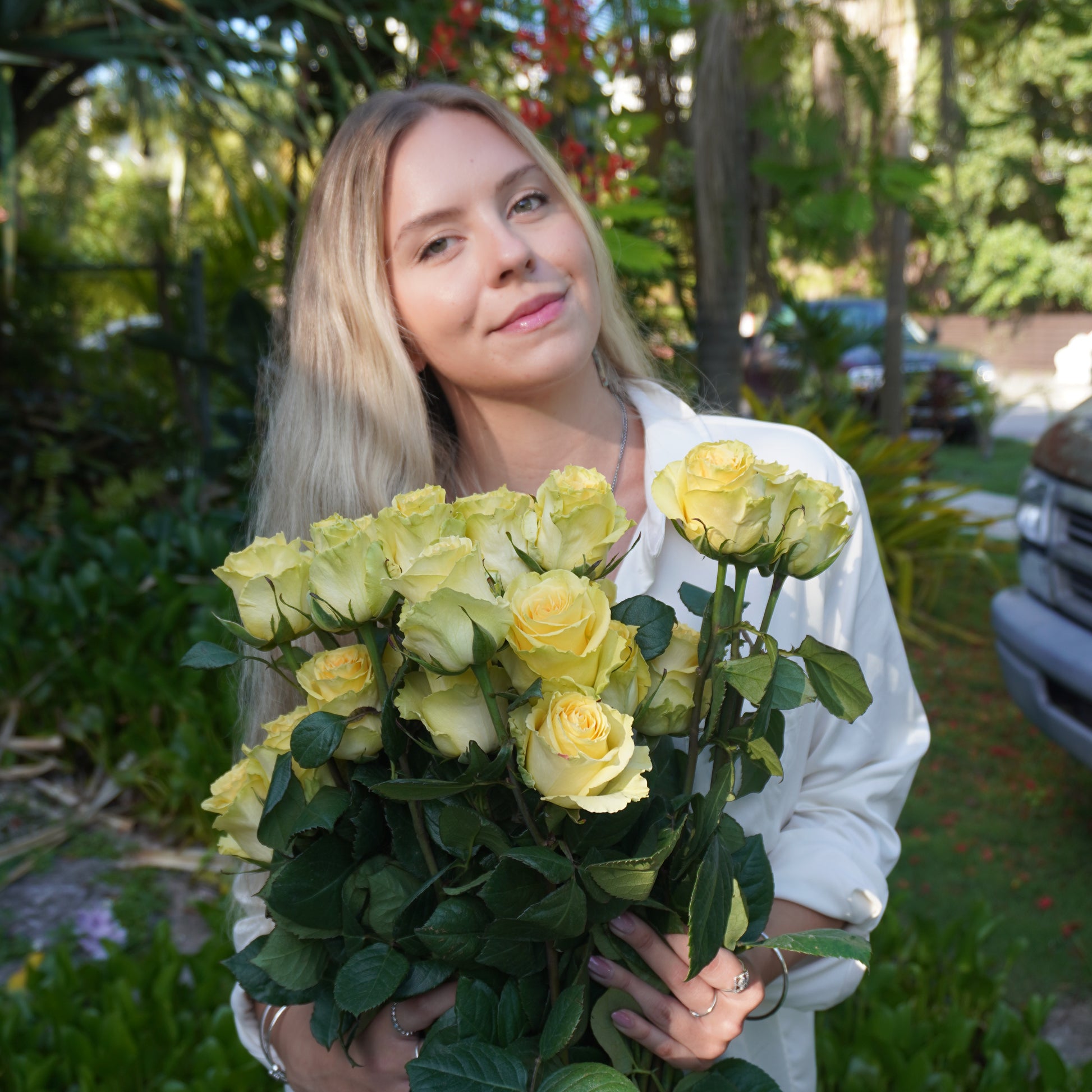 Woman holding a bouquet of yellow flowers outdoors with greenery in the background
