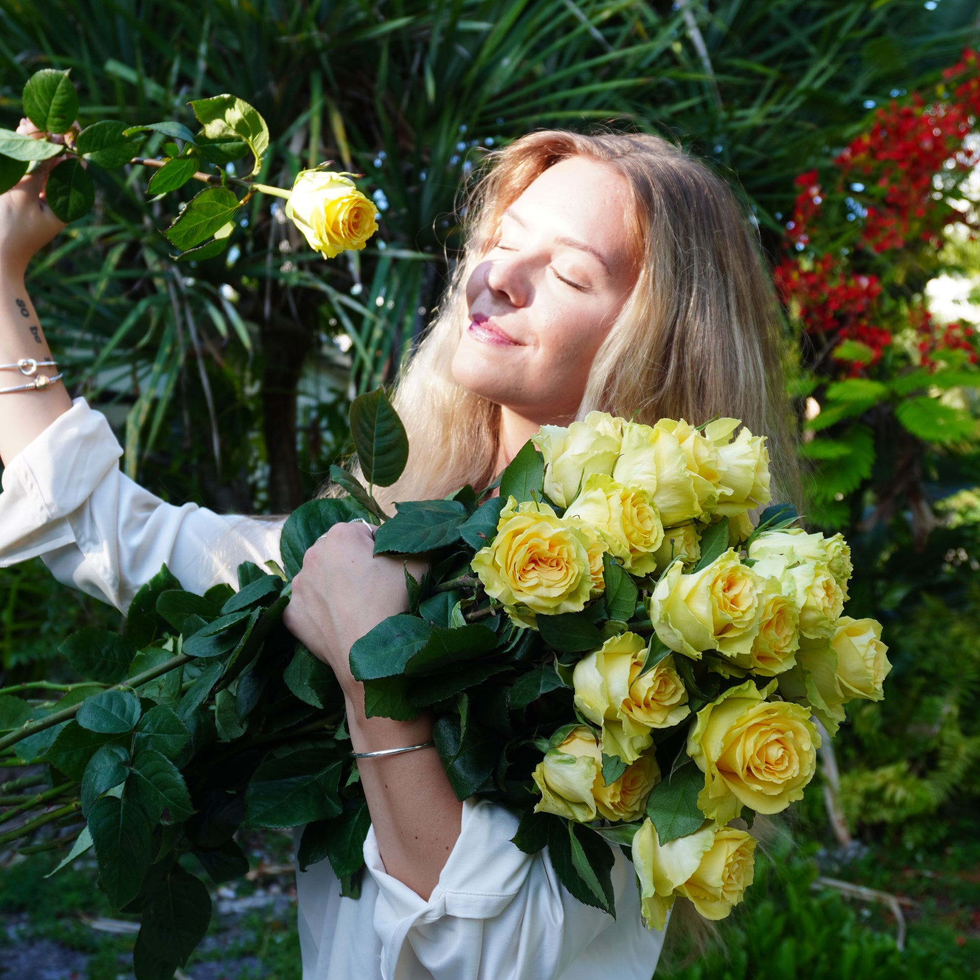 Person holding a bouquet of yellow roses with greenery in the background