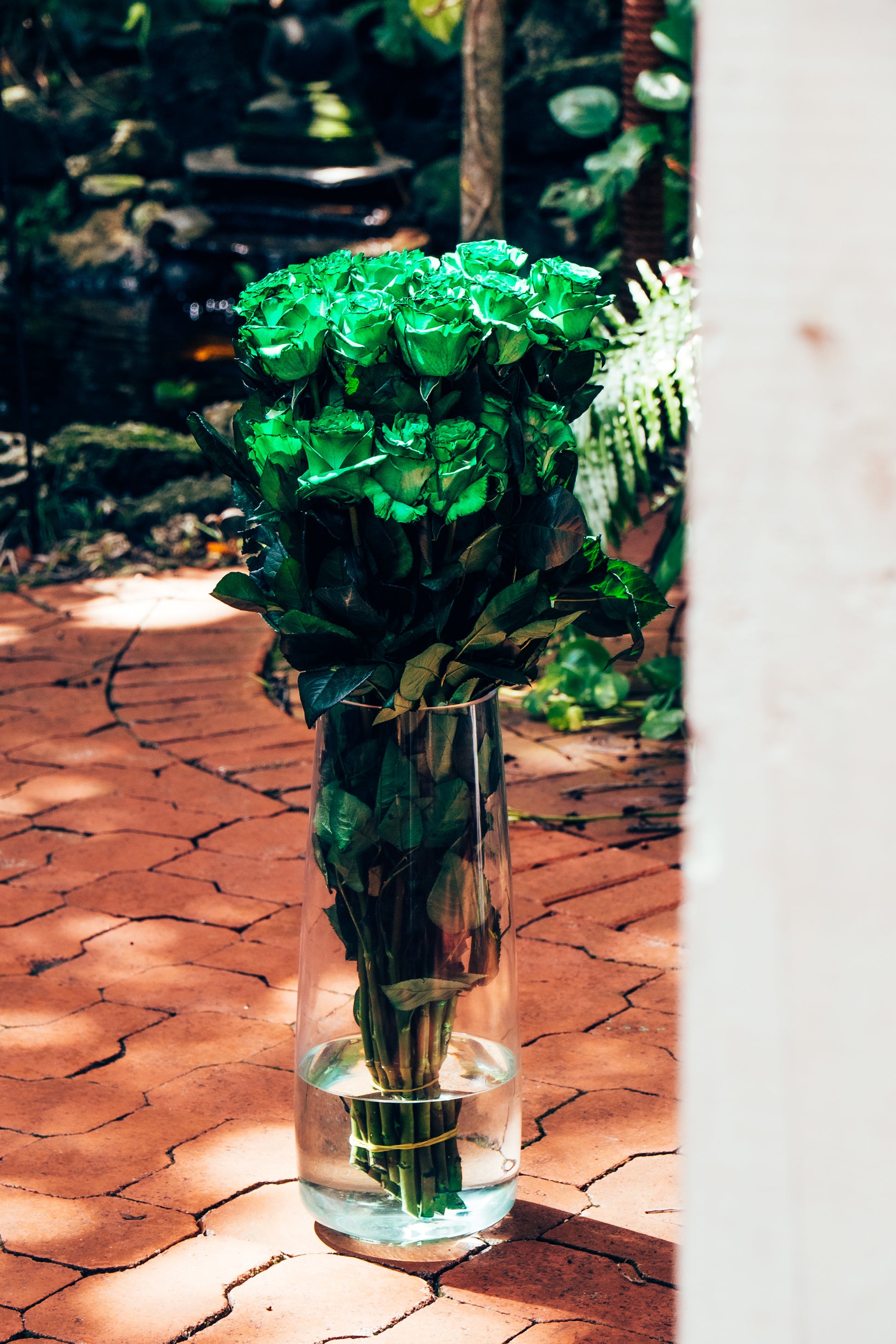 Bouquet of green roses in a clear vase on a brick path