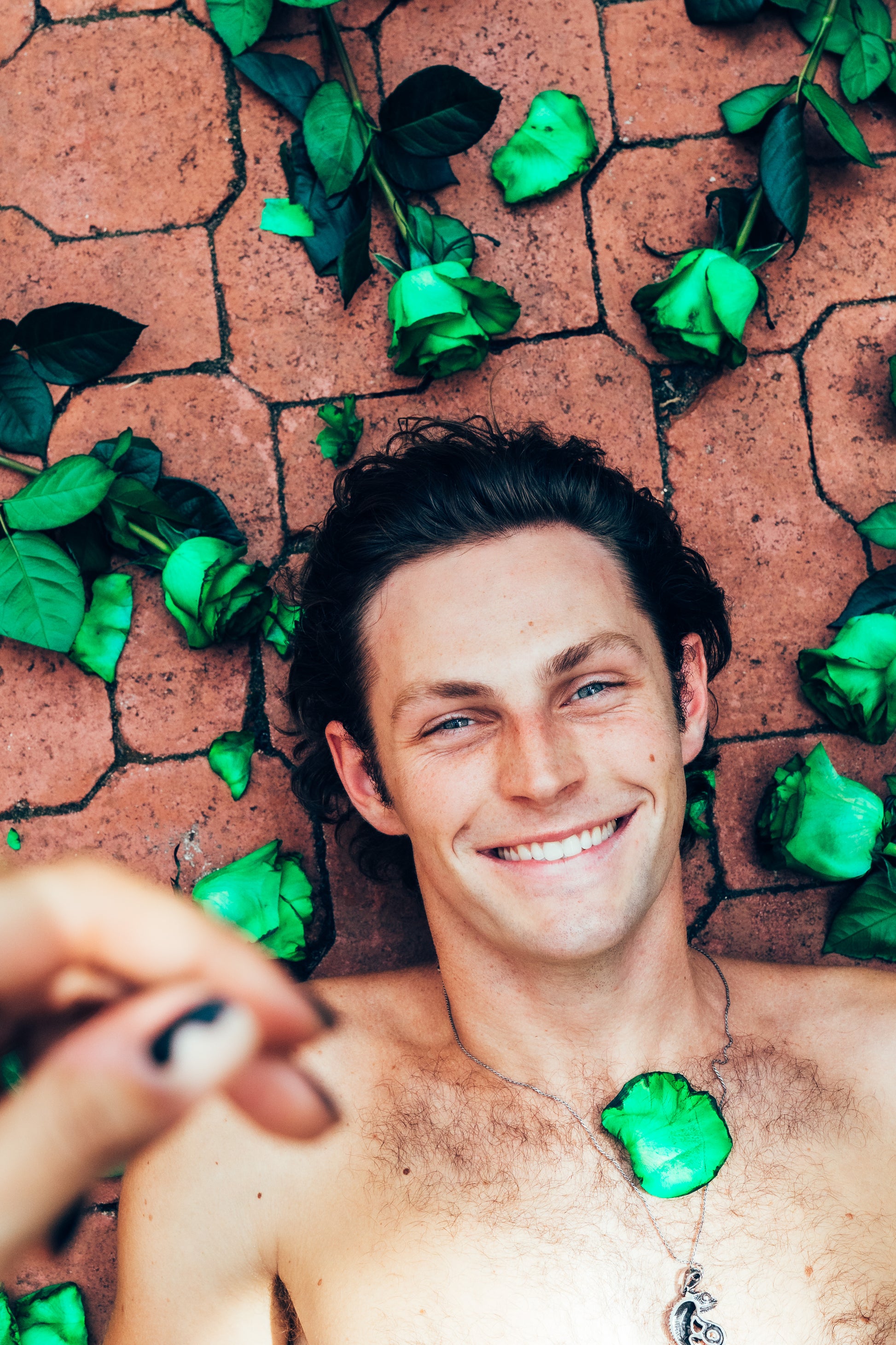 Man lying on a brick surface with green leaves around, holding a camera.