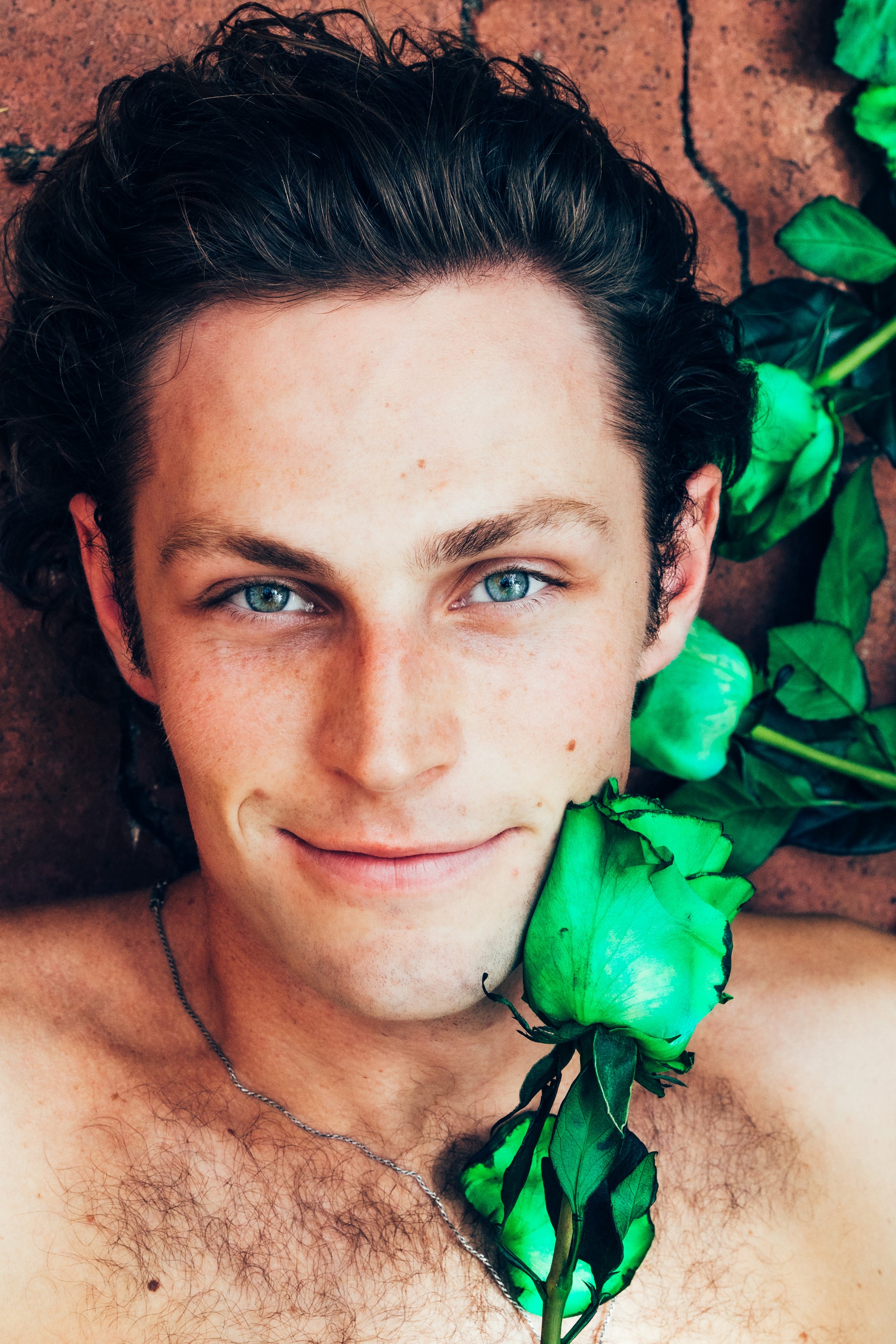 Man with green roses around his neck against a brick floor