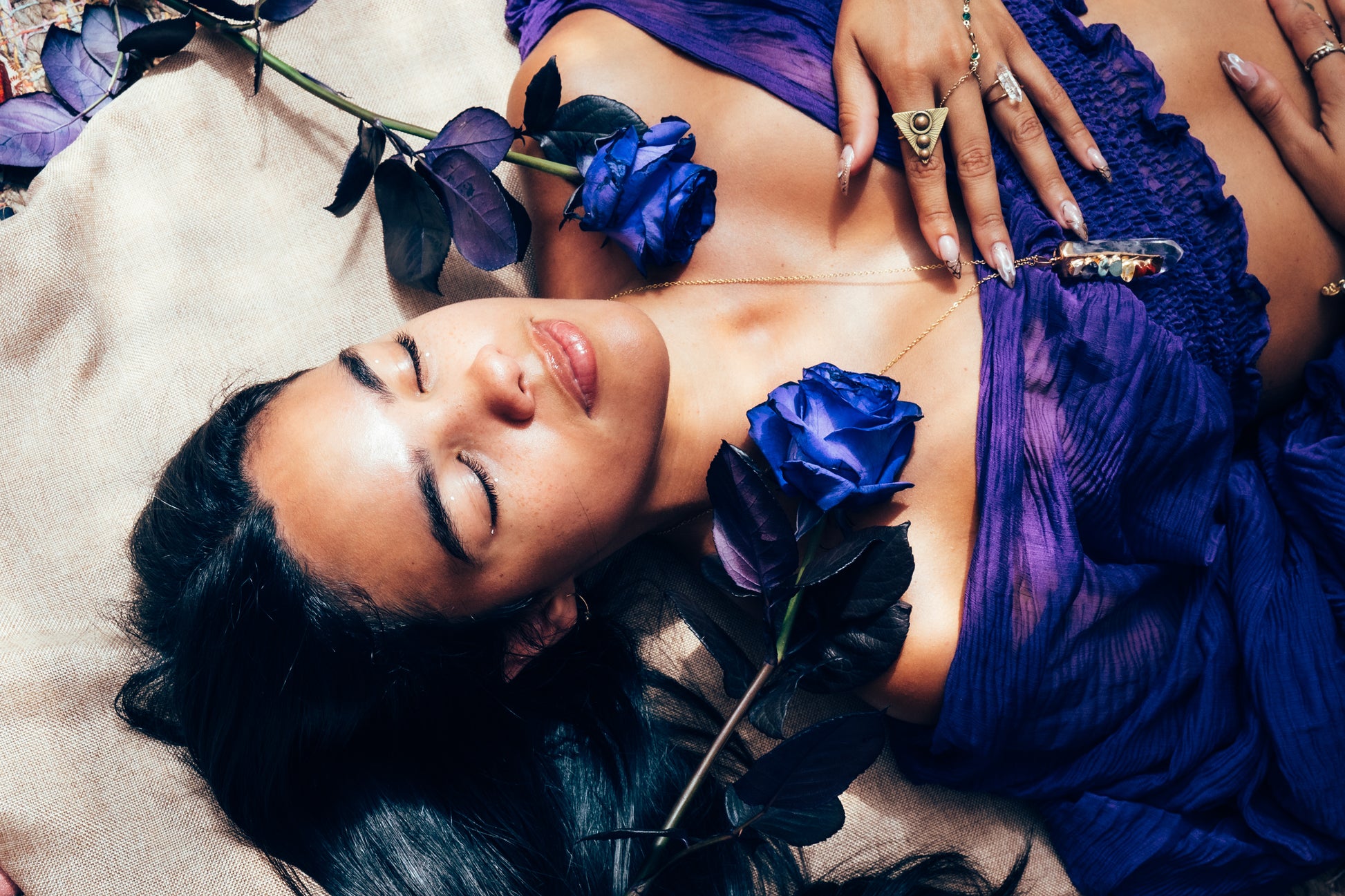 Woman in a purple dress lying on a beige surface with blue flowers.