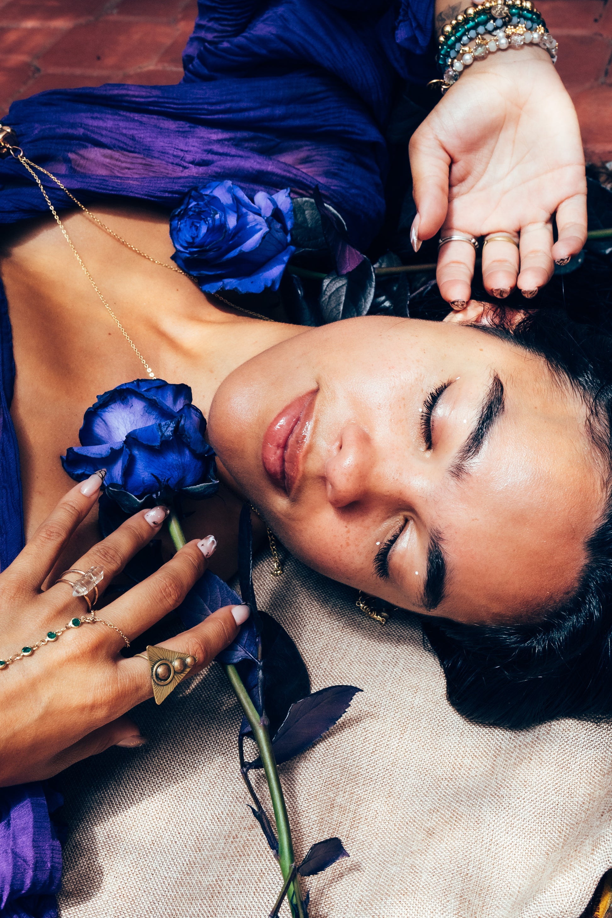 Woman lying down with blue flowers and jewelry, wearing a blue dress.
