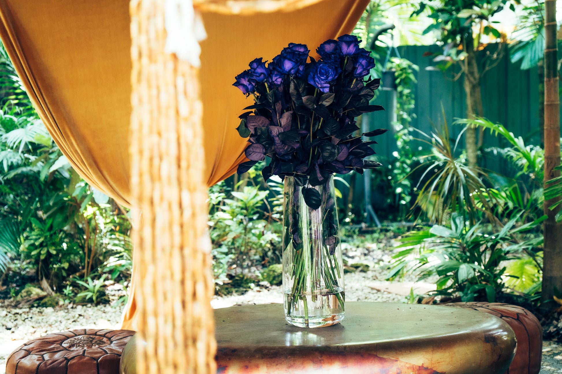 Bouquet of purple roses in a clear vase on a wooden table with a garden background
