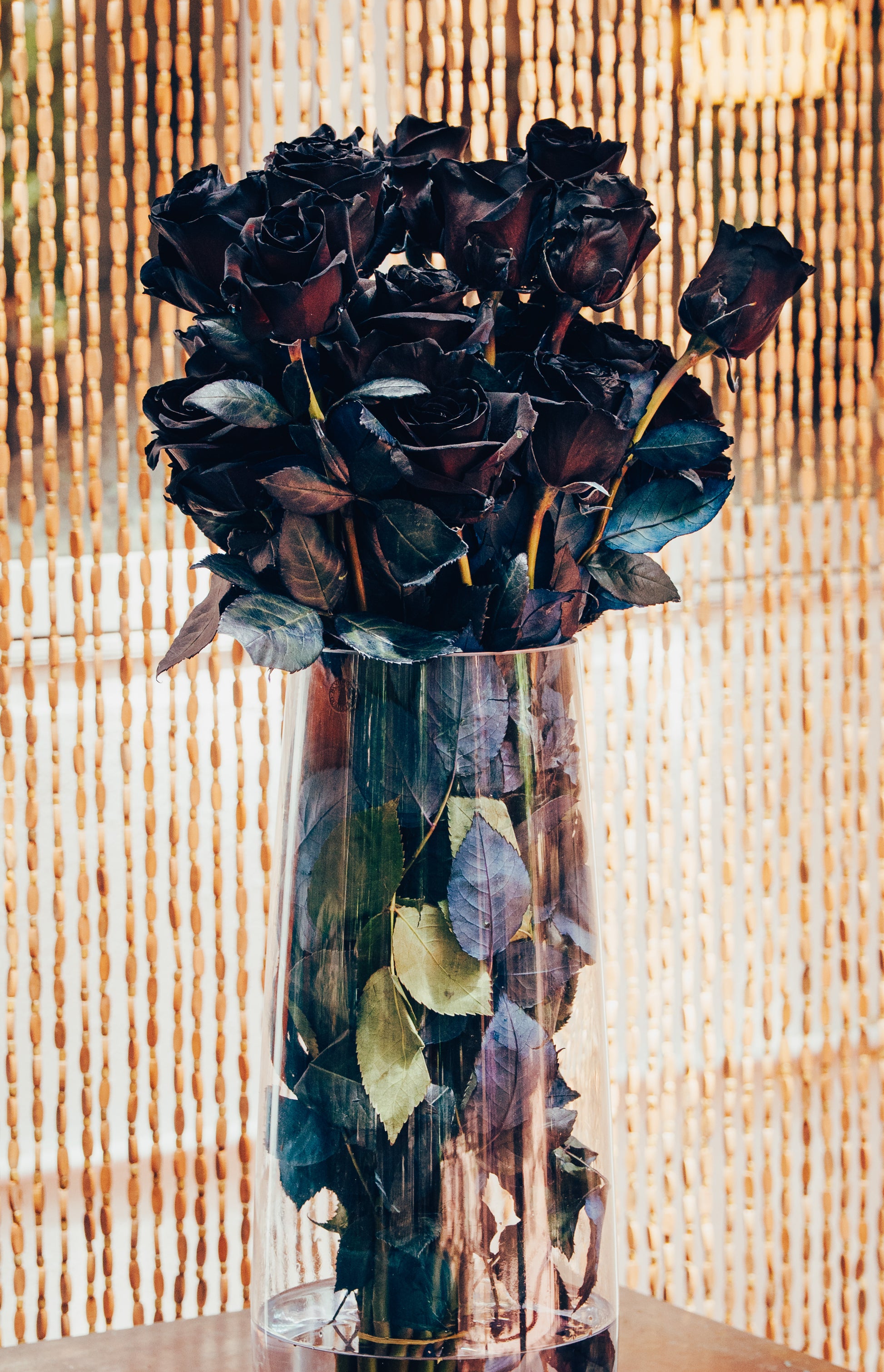 Bouquet of black roses in a clear vase against a woven background