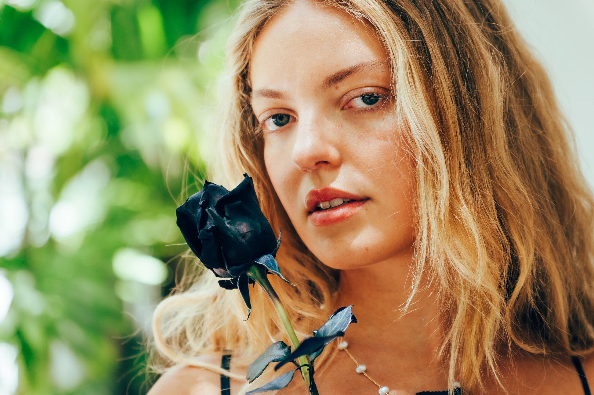 Woman holding a black rose with blurred greenery in the background