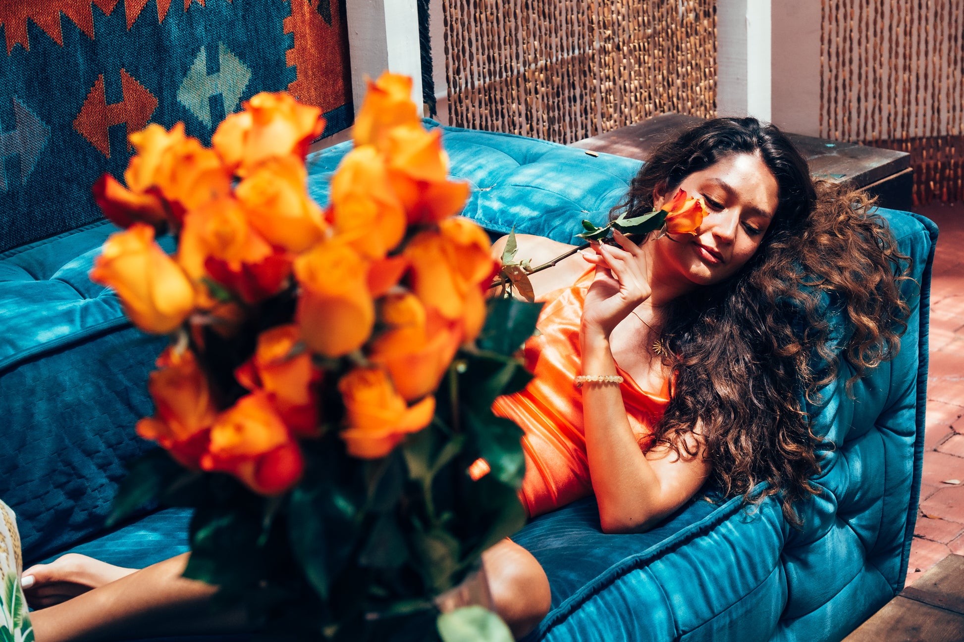 Woman sitting on a blue couch with orange flowers and a colorful blanket in the background
