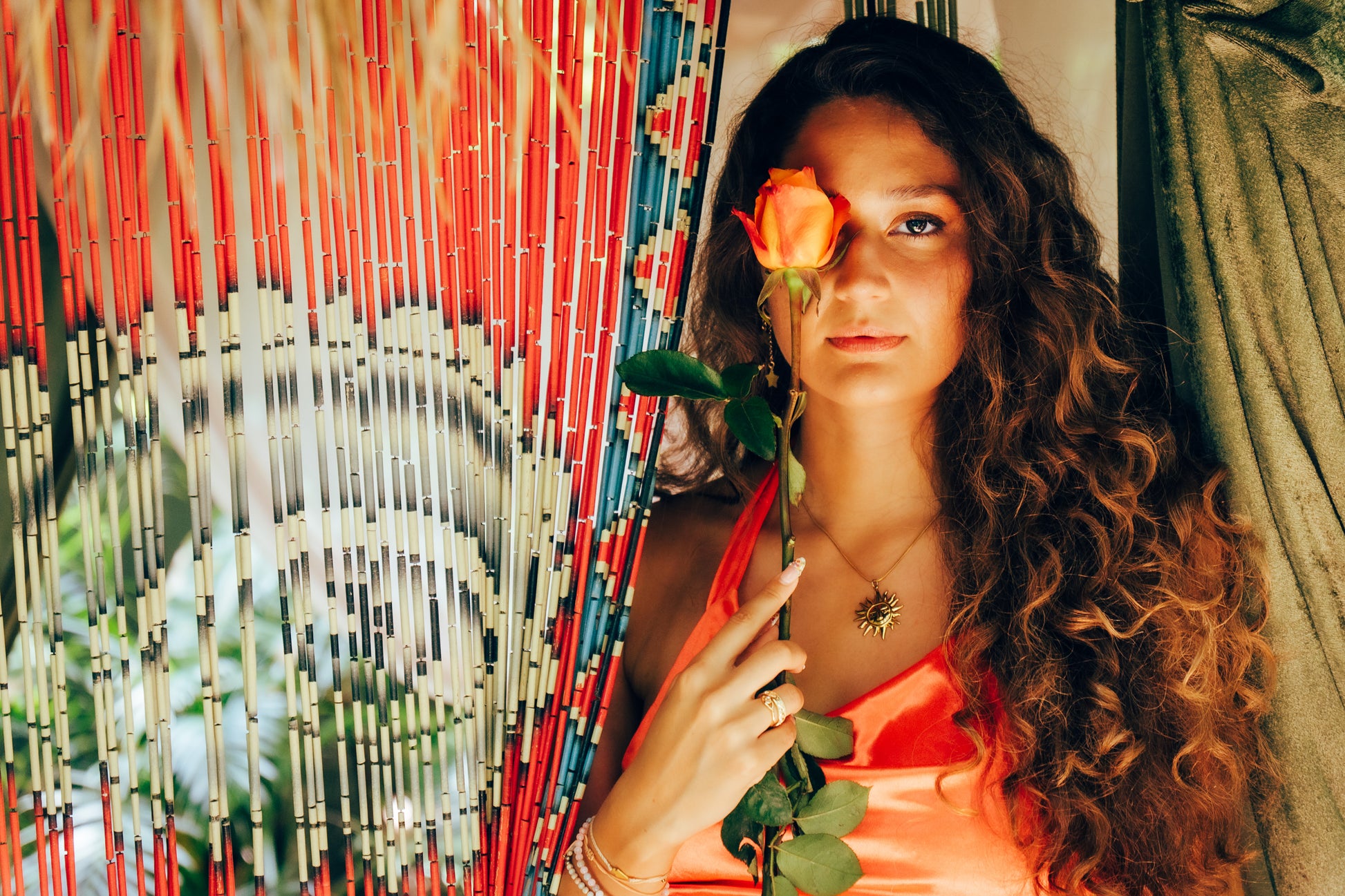 Woman holding a rose in front of a colorful woven wall.