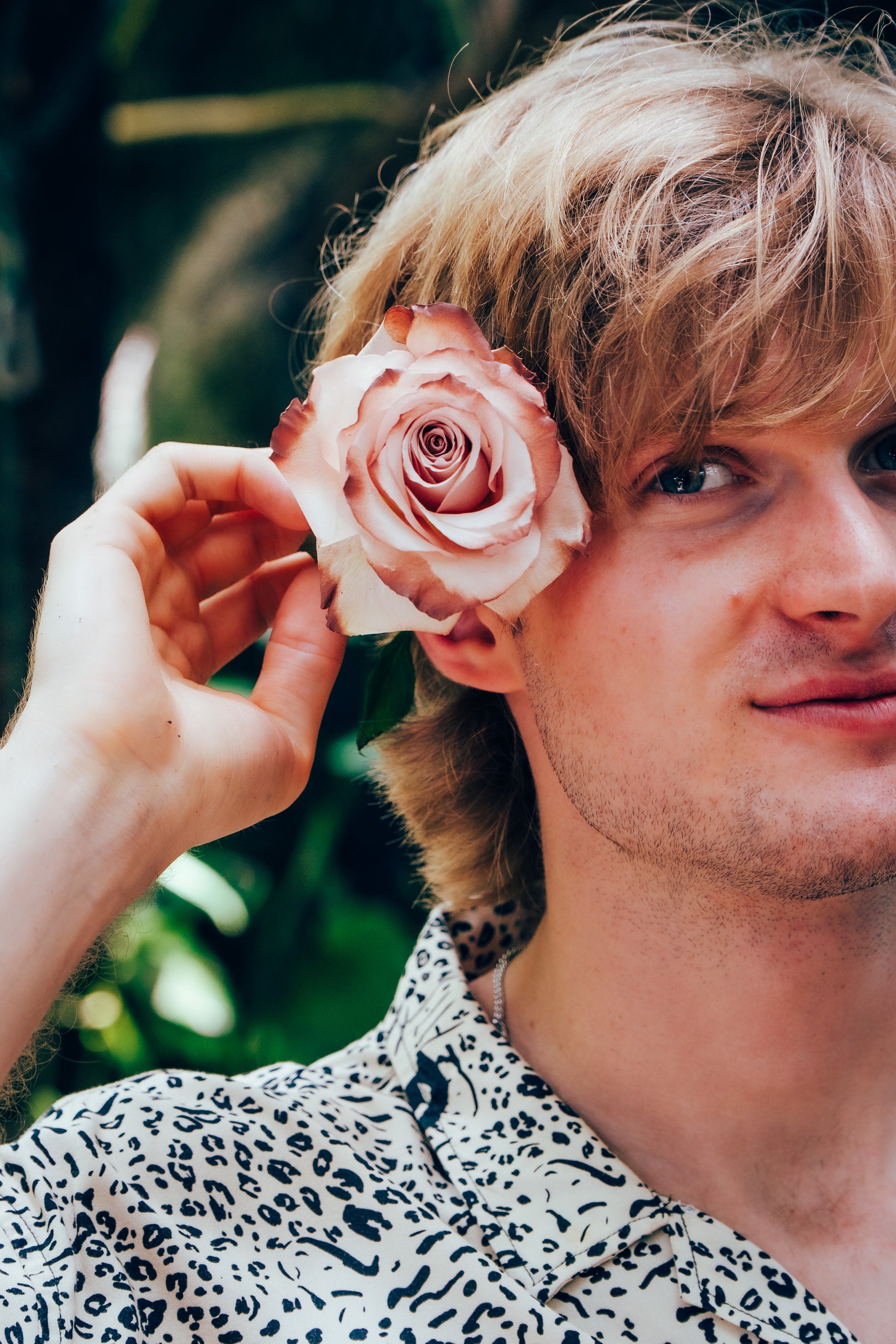 Man with a pink rose in his hair against a blurred green background