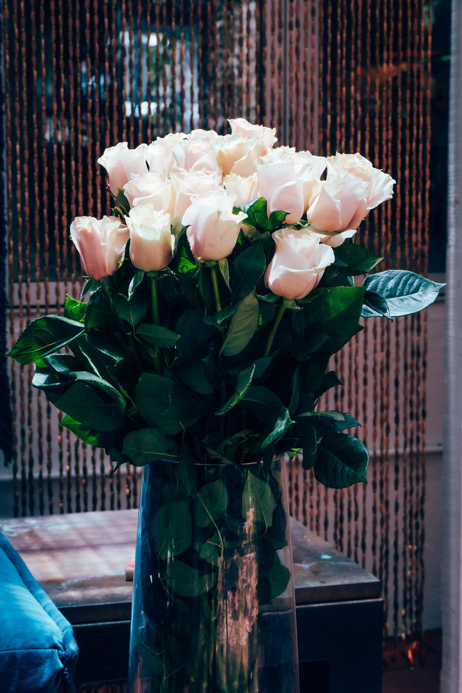 Bouquet of pink roses in a clear vase on a reflective surface with a blurred background.