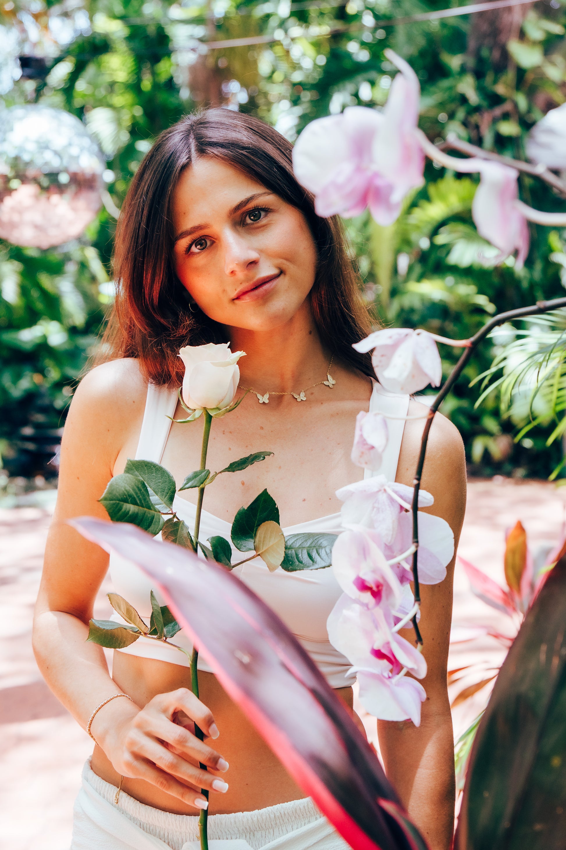 Woman holding a pink rose in a garden with pink flowers and greenery