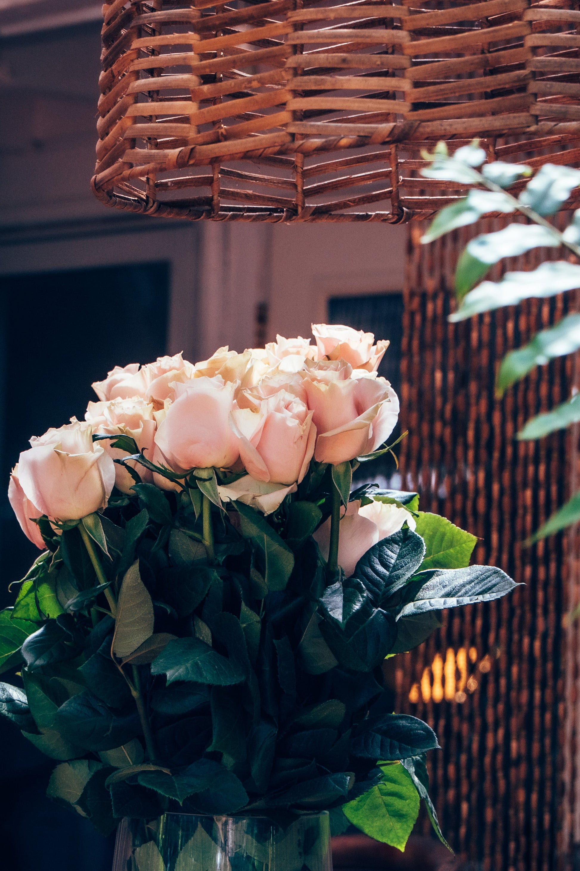 Bouquet of pink roses in a clear vase with a wicker basket in the background.