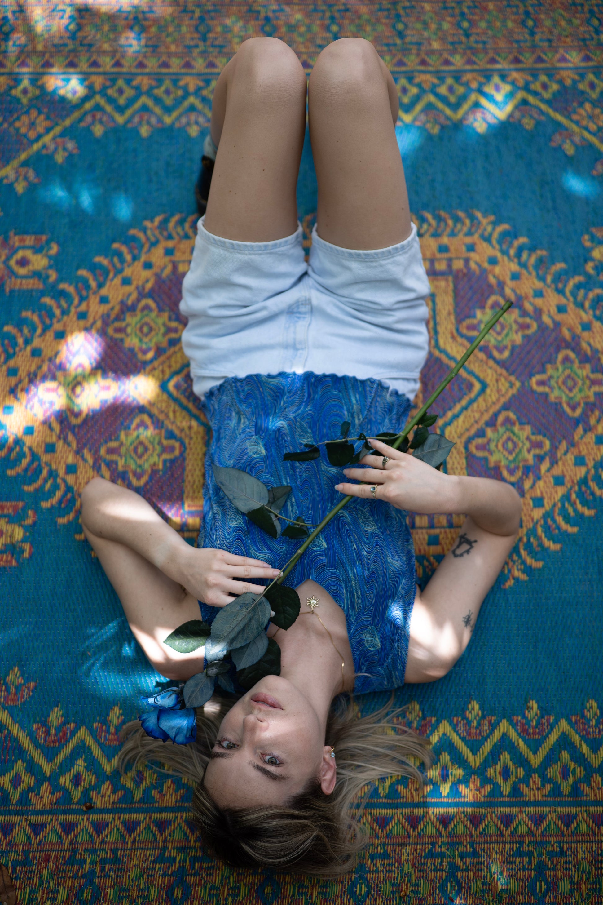Person lying on a colorful patterned rug with flowers and sunglasses.