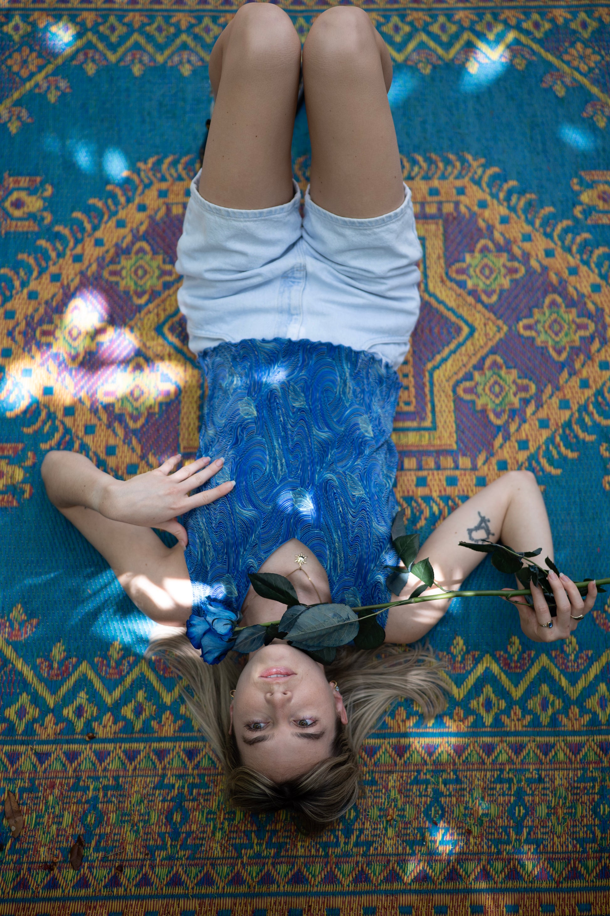 Person lying on a colorful patterned rug holding a blue rose