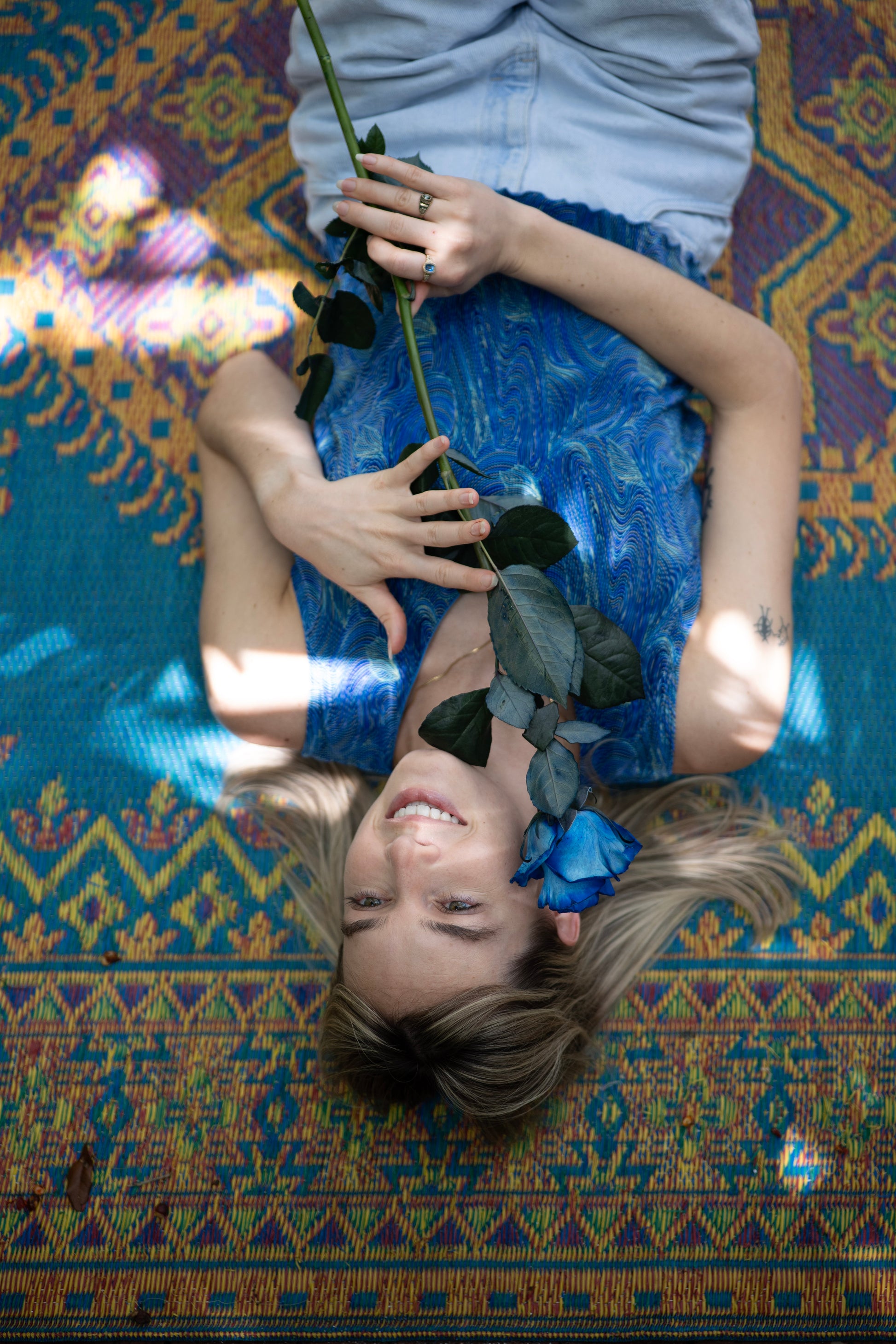 Person lying on a colorful patterned rug holding a blue rose