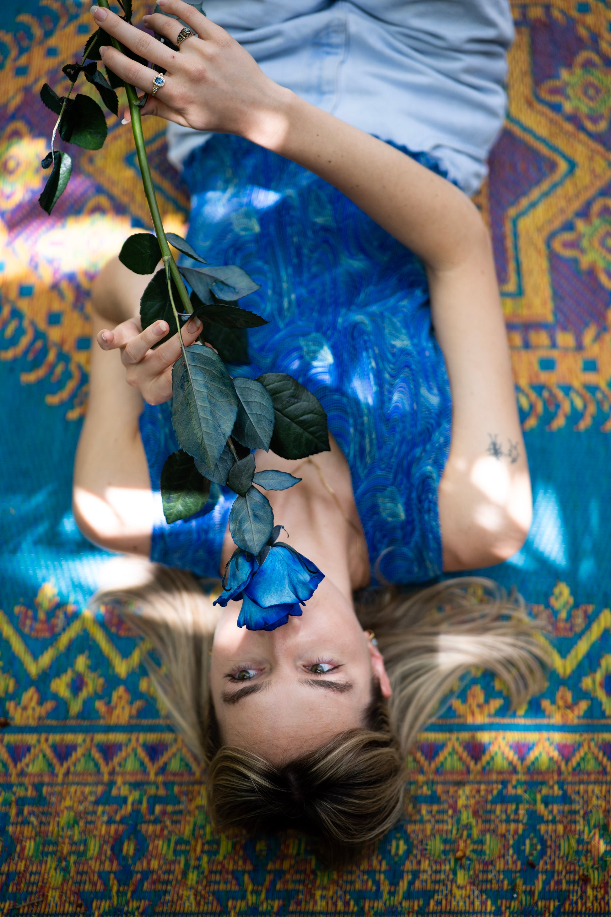 Person lying on a colorful patterned rug holding a blue flower