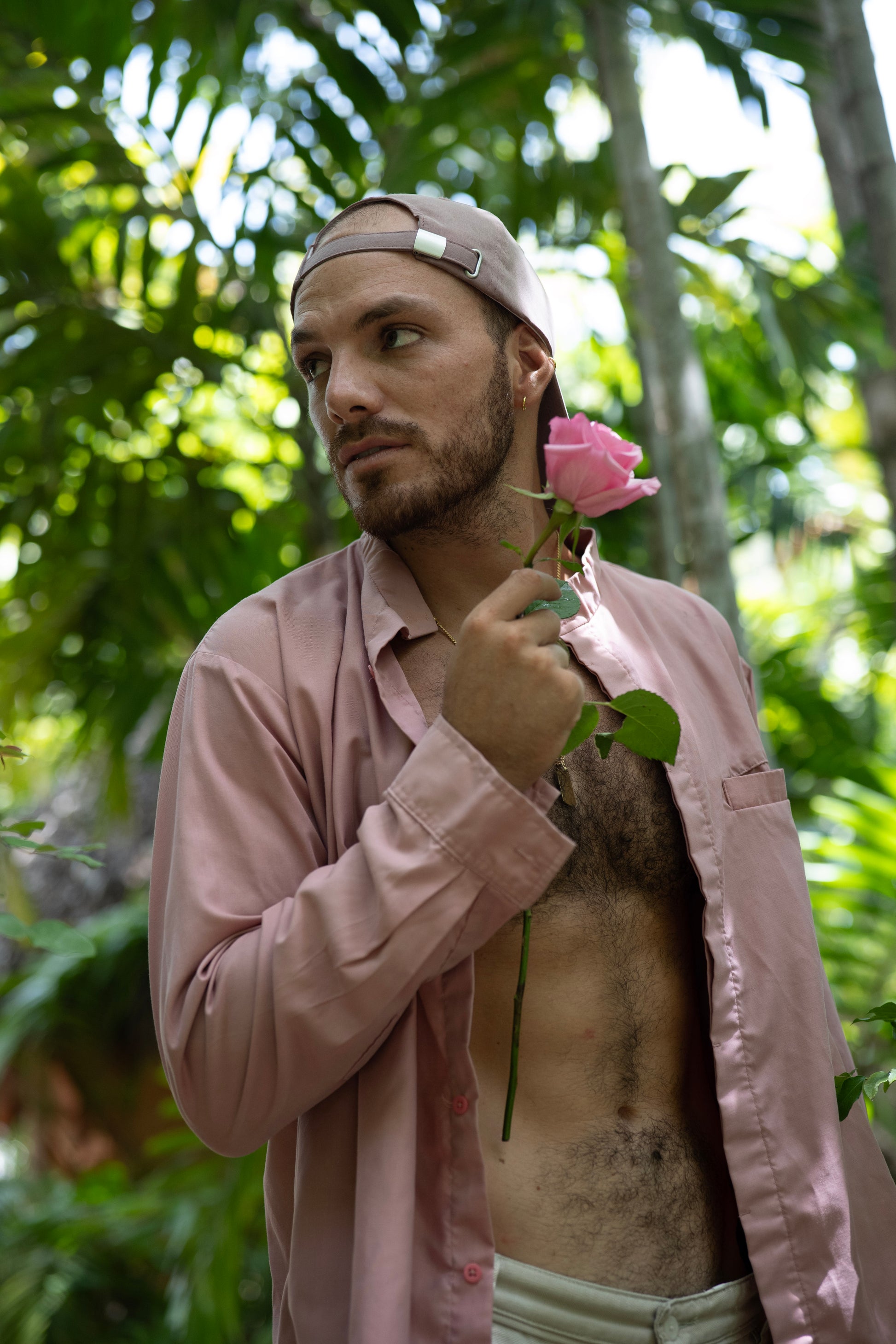 Man holding a pink rose in a tropical setting