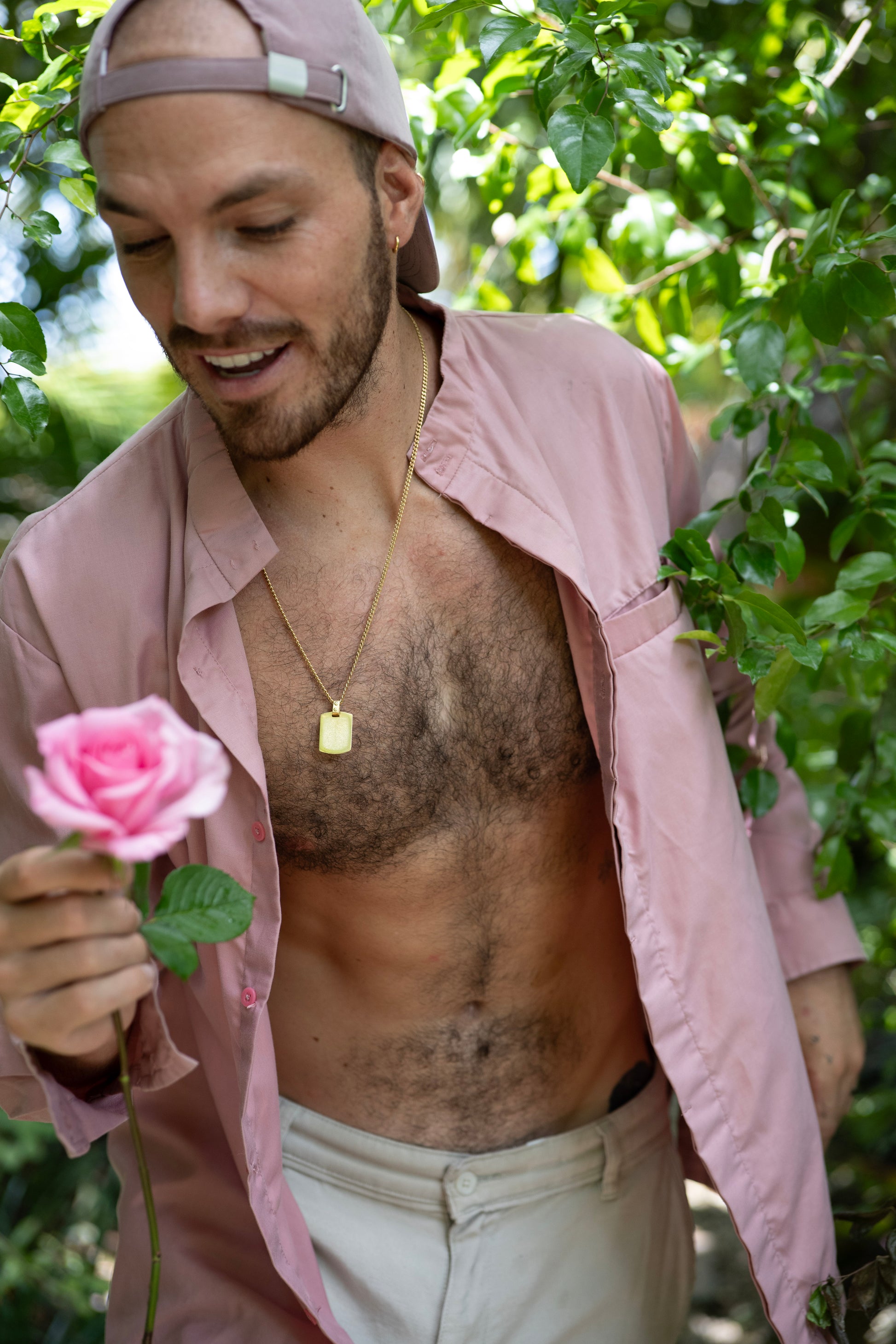 Man holding a pink rose outdoors with greenery in the background