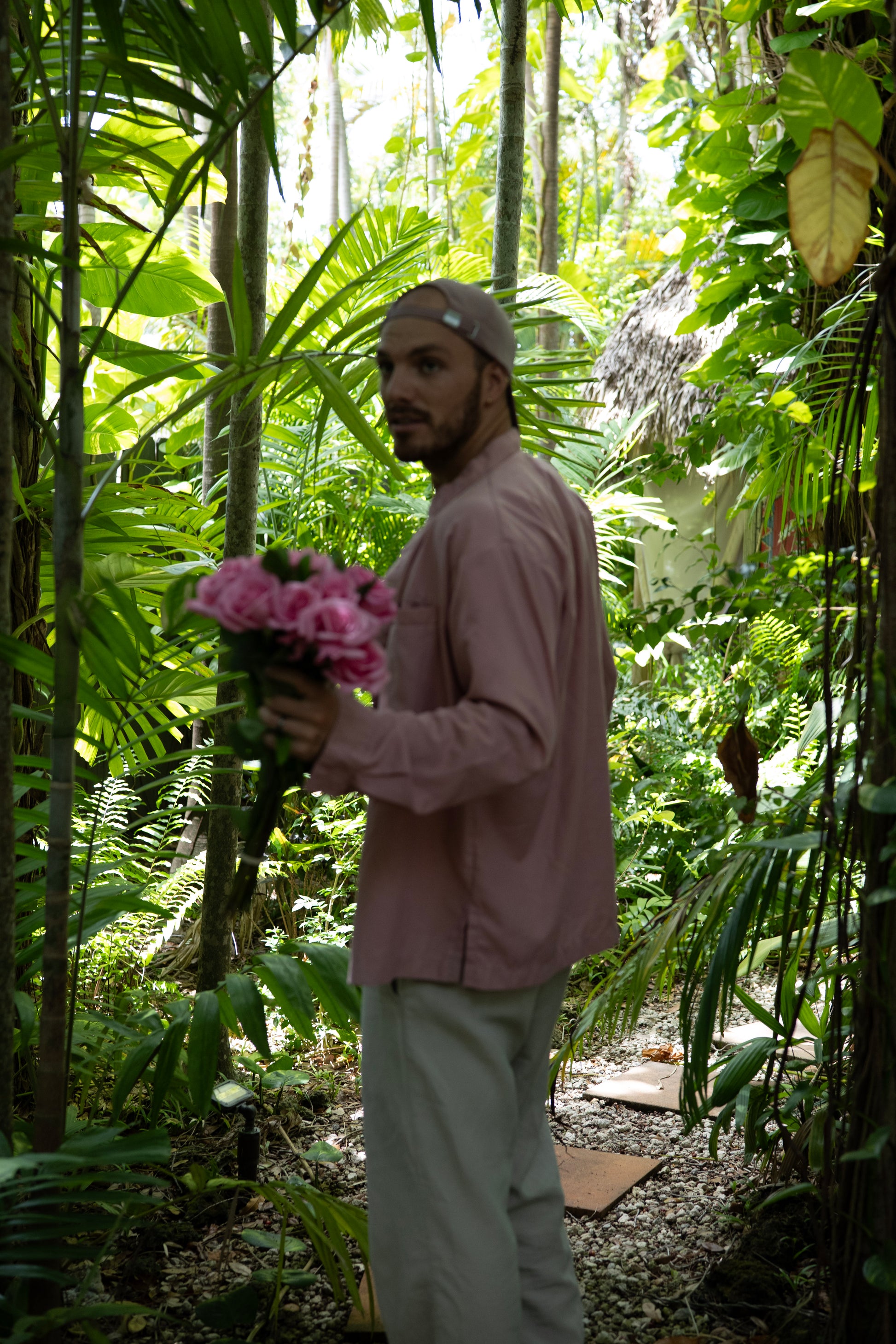 Man holding pink flowers in a lush green forest