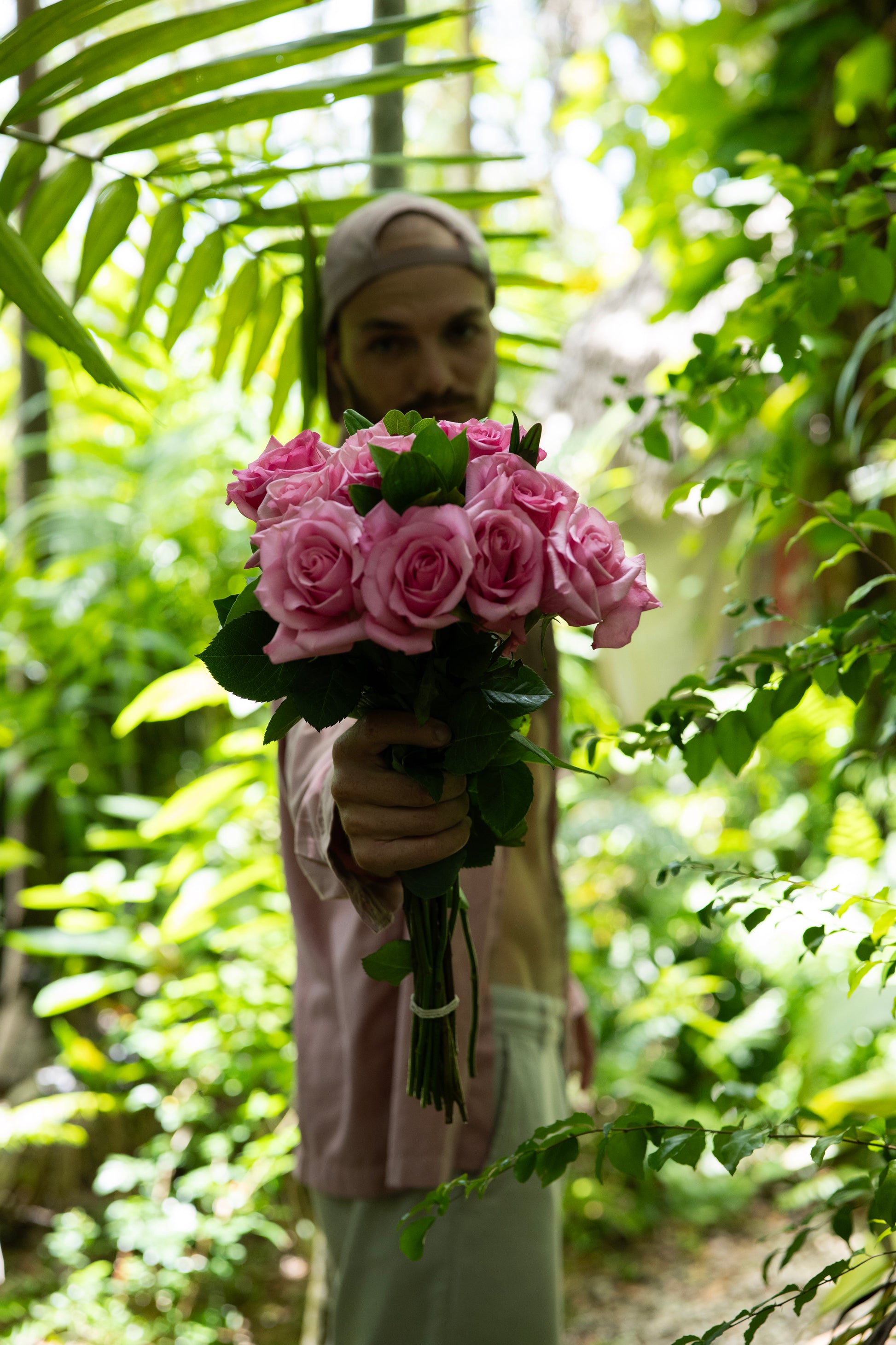 Person holding a bouquet of pink flowers amidst green foliage