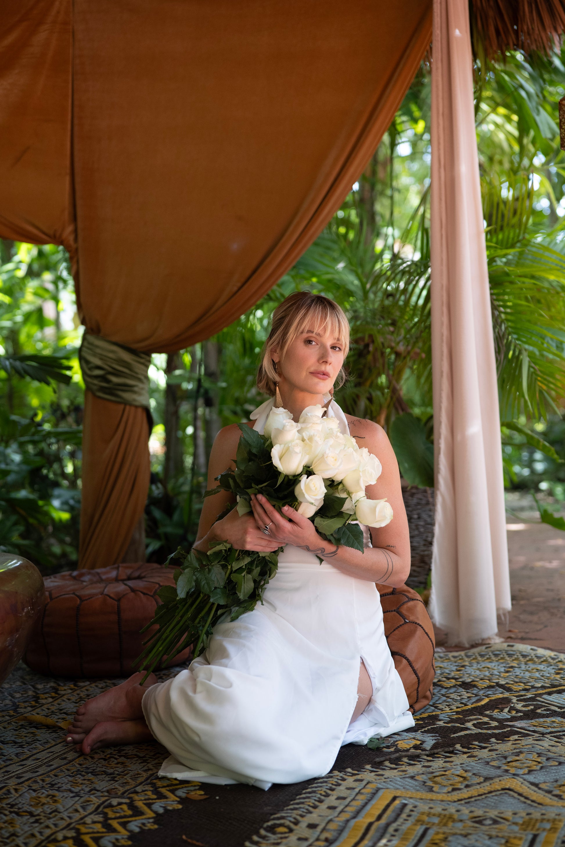 Woman in a white dress holding roses under a canopy with greenery in the background