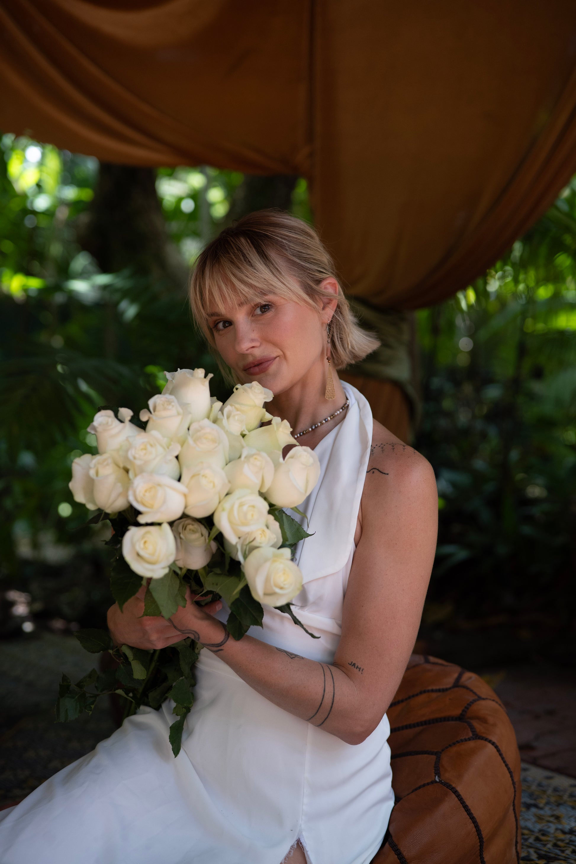 Woman in a white dress holding a bouquet of white roses in a natural setting.