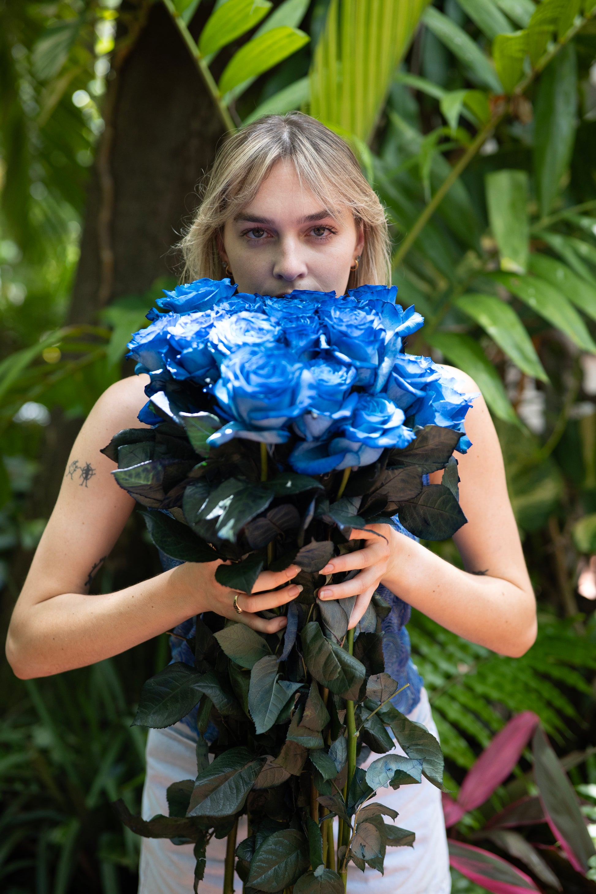 Person holding a large bouquet of blue roses in front of a green leafy background