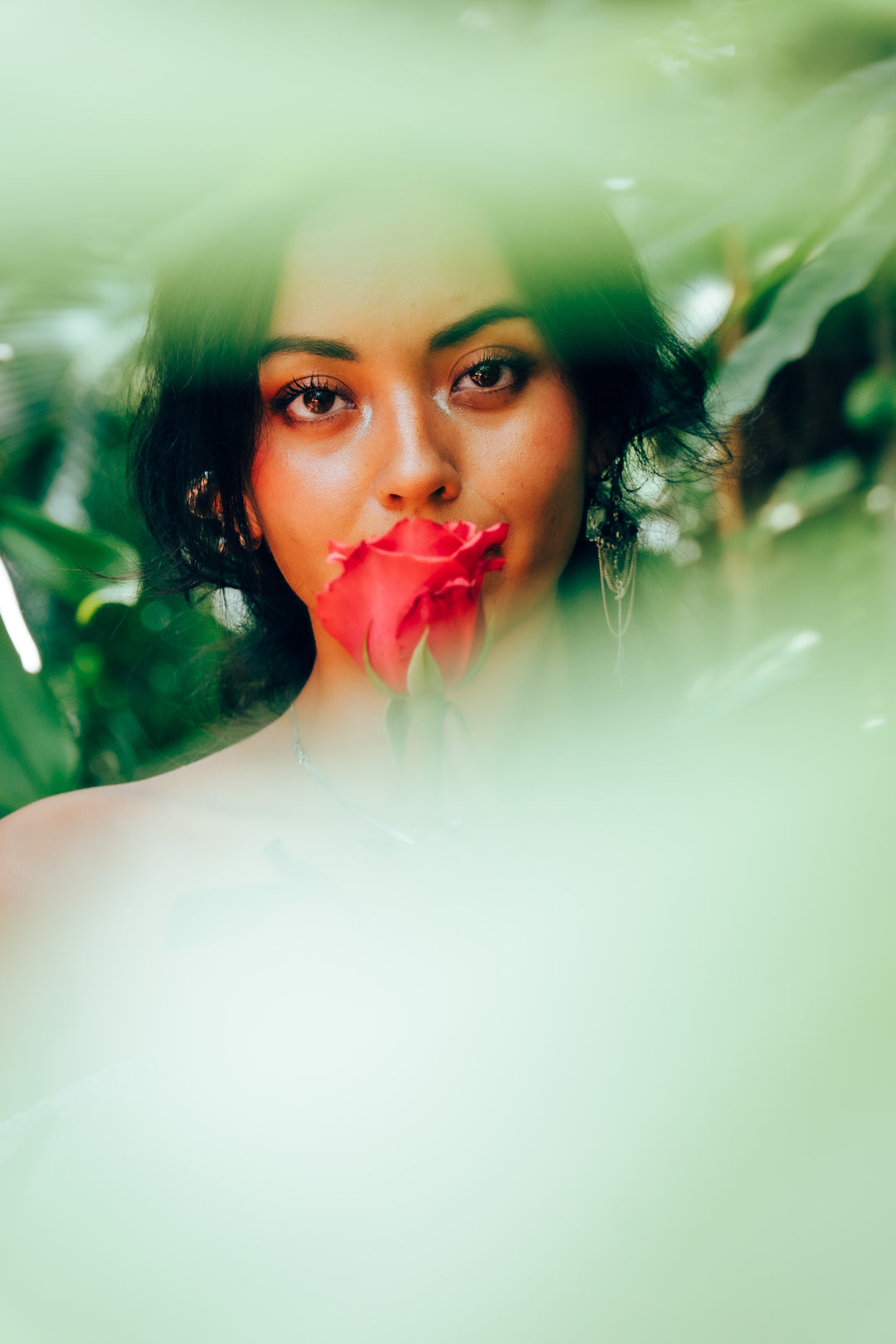 Woman holding a hot pink rose behind green foliage