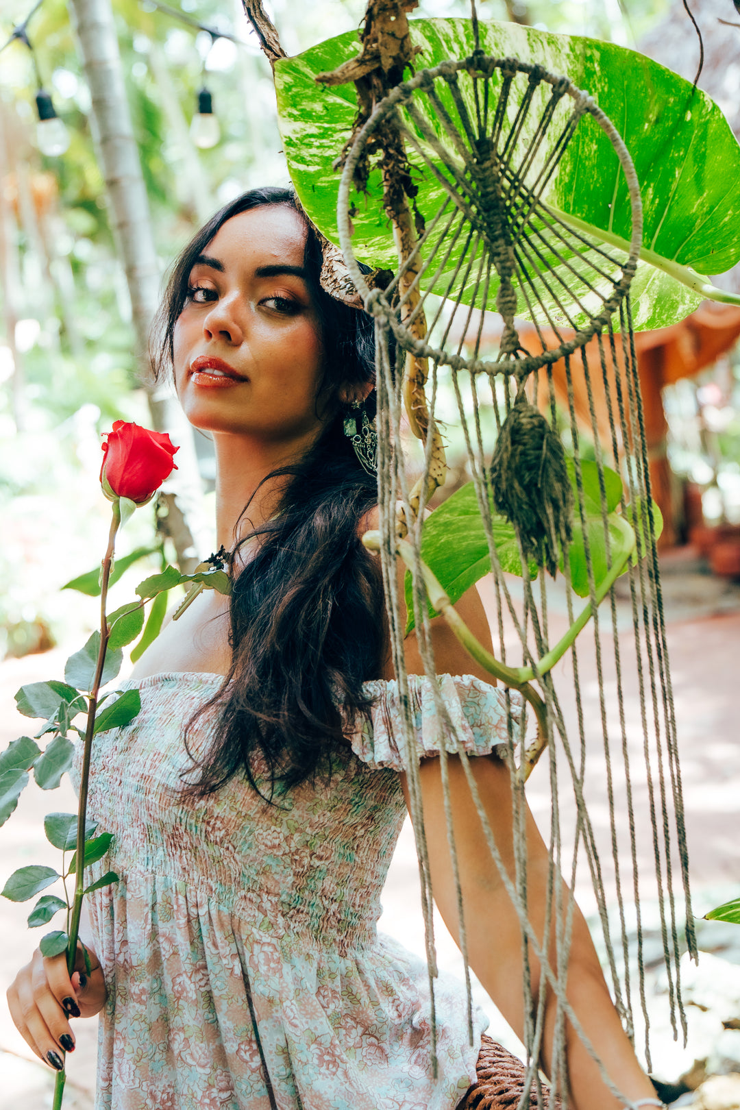 Woman holding a hot pink rose with a macrame hanging and green leaves in the background