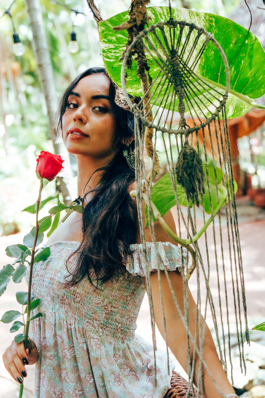 Woman holding a hot pink rose with a macrame hanging and green leaves in the background