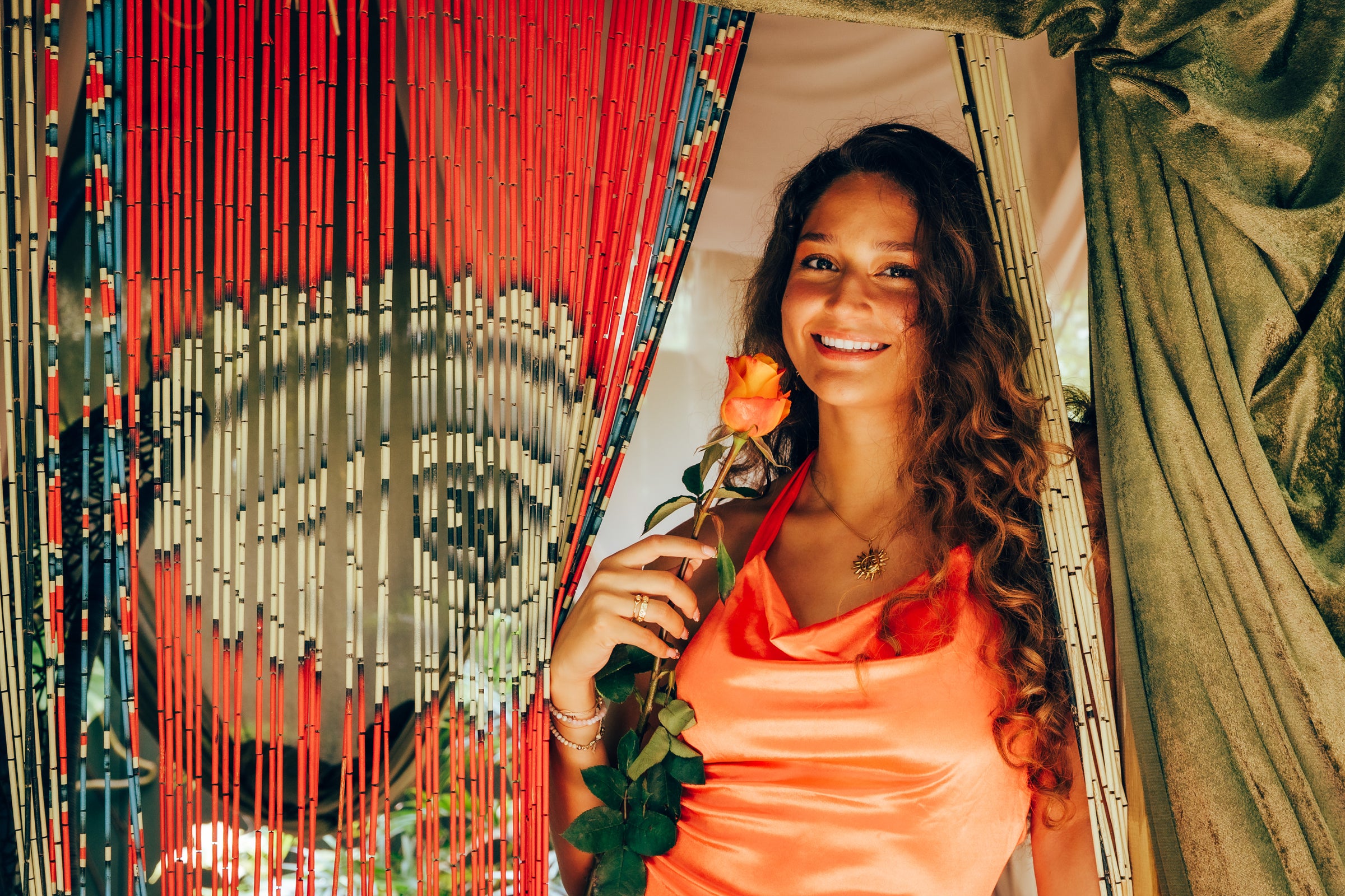 Woman holding a rose in front of a decorative curtain with red strings.