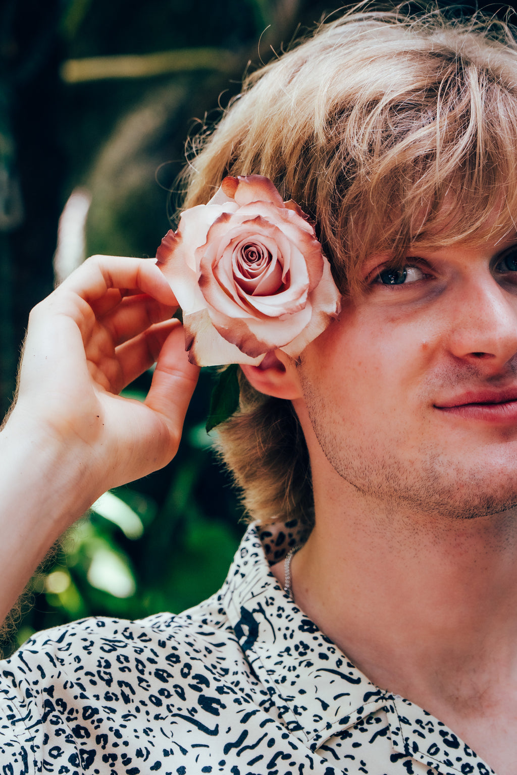 Man with a pink rose in his hair against a blurred green background