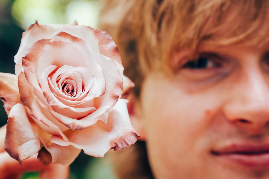 Close-up of a pink rose held close to a person's face with a blurred background