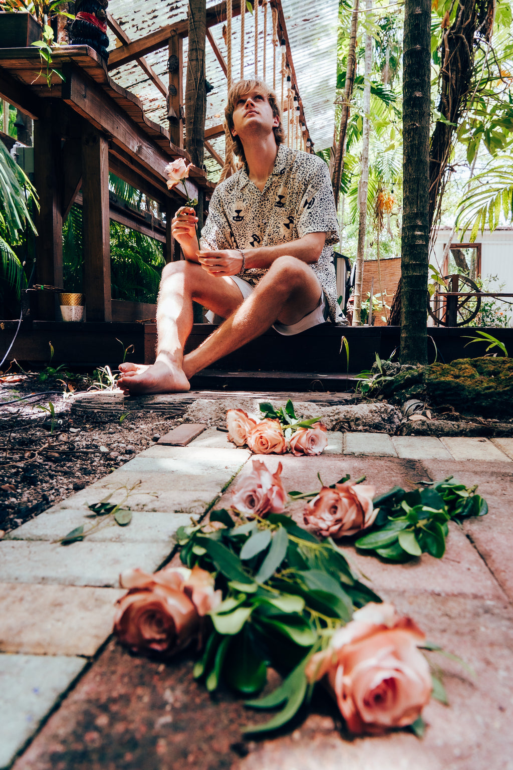 Person sitting on a wooden deck with flowers in a garden setting