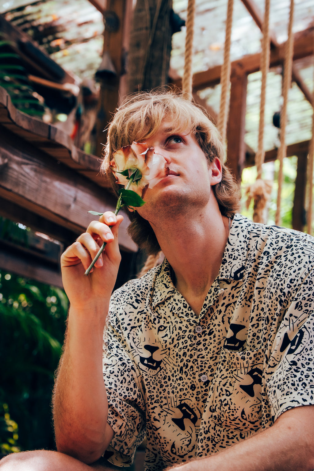 Person holding a flower to their face in an outdoor setting with wooden beams and greenery.